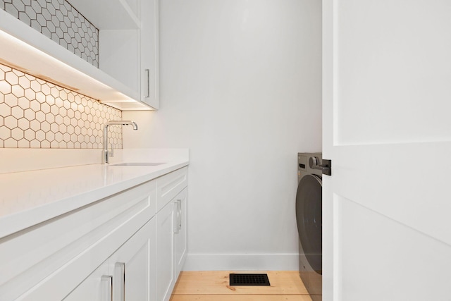 washroom with cabinet space, a sink, washer / dryer, light wood-type flooring, and baseboards