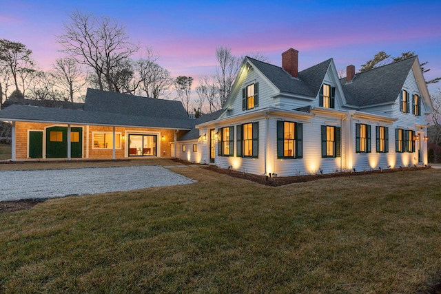 back of property at dusk with a shingled roof, a patio area, a lawn, and a chimney