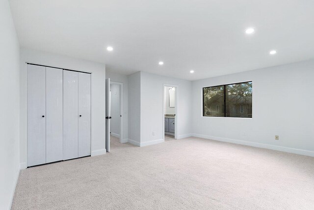 unfurnished bedroom featuring connected bathroom, a closet, and light carpet