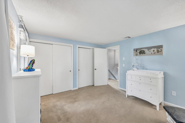 bedroom with light colored carpet, a textured ceiling, and multiple closets