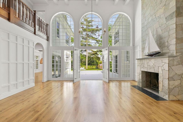 unfurnished living room with a towering ceiling, a stone fireplace, french doors, hardwood / wood-style flooring, and beam ceiling