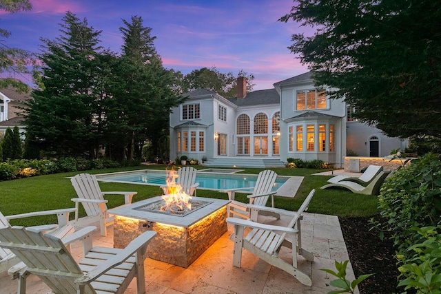 back house at dusk featuring a patio, a yard, and a fire pit