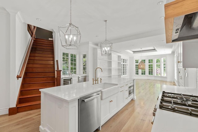 kitchen featuring dishwasher, a kitchen island with sink, white cabinets, sink, and pendant lighting