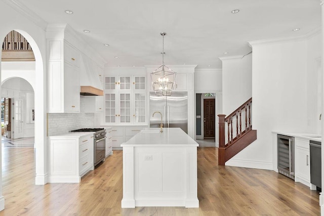 kitchen featuring premium appliances, white cabinetry, hanging light fixtures, a kitchen island with sink, and beverage cooler