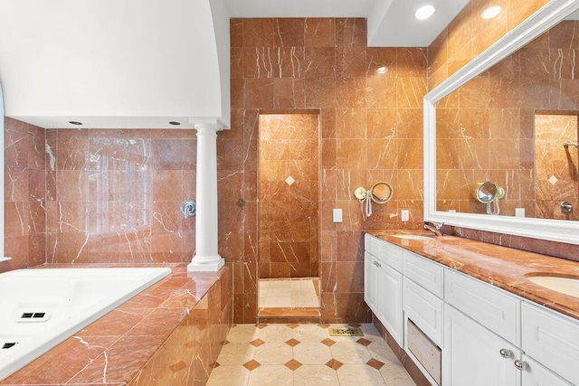 bathroom with decorative columns, tiled tub, tile walls, and vanity