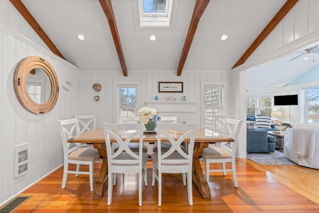 dining area featuring heating unit, lofted ceiling with skylight, and light hardwood / wood-style flooring