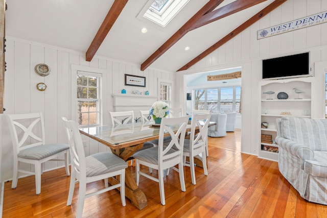 dining area with built in shelves, light hardwood / wood-style flooring, and vaulted ceiling with skylight