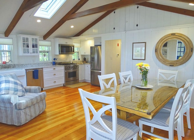 dining space with light hardwood / wood-style floors and vaulted ceiling with skylight