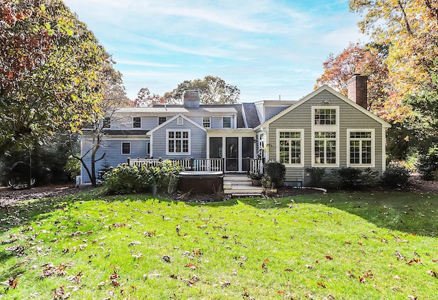 rear view of house with a sunroom, a lawn, and a hot tub