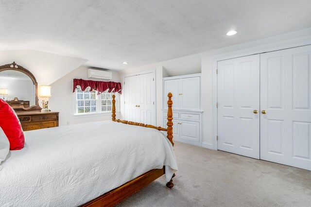 bedroom with light carpet, two closets, a wall unit AC, and vaulted ceiling