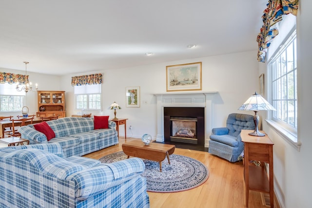 living area featuring baseboards, a fireplace with flush hearth, an inviting chandelier, and wood finished floors