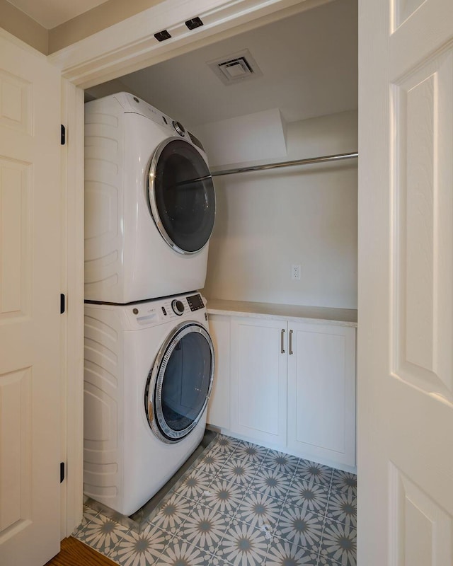 laundry area with laundry area, stacked washing maching and dryer, visible vents, and light floors