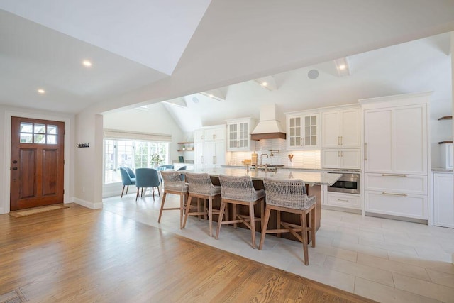 kitchen with lofted ceiling, stainless steel oven, a breakfast bar area, white cabinetry, and custom range hood