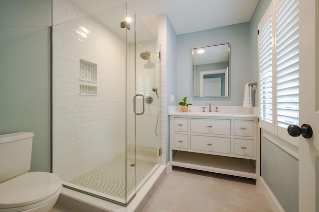 bathroom featuring tile patterned flooring, a stall shower, vanity, baseboards, and toilet