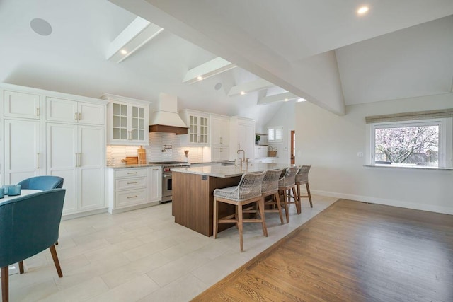 kitchen with stainless steel stove, a kitchen breakfast bar, tasteful backsplash, custom range hood, and lofted ceiling with beams
