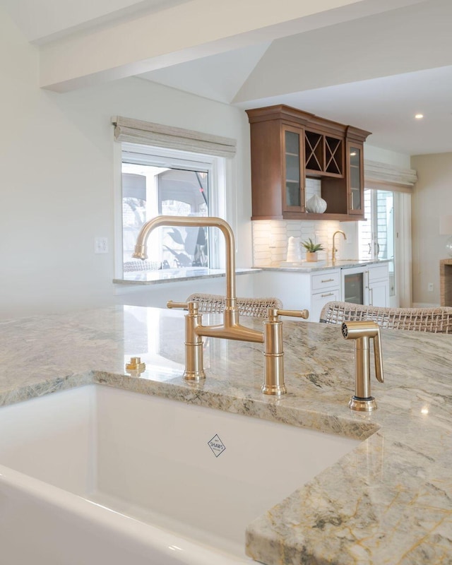 kitchen featuring wine cooler, light stone countertops, glass insert cabinets, tasteful backsplash, and a sink