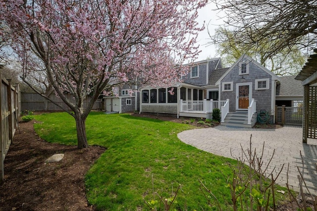 rear view of house with a lawn, a sunroom, a patio area, a fenced backyard, and a shingled roof
