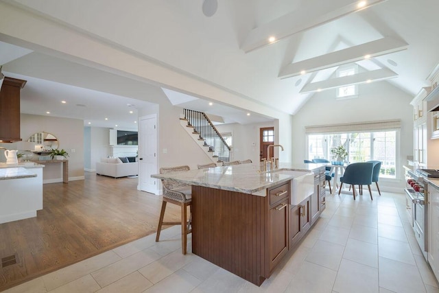 kitchen featuring open floor plan, an island with sink, a breakfast bar area, light stone counters, and a sink