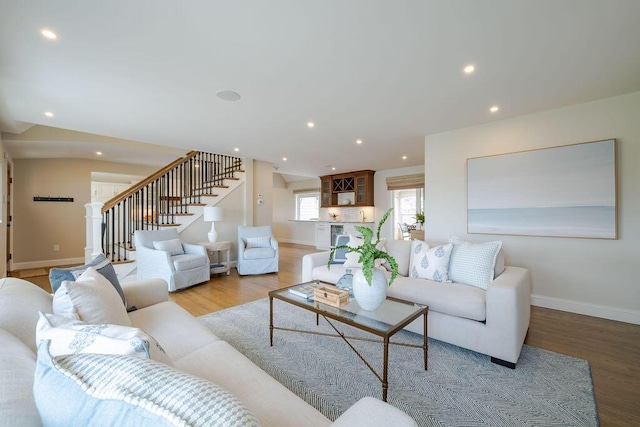 living area with recessed lighting, baseboards, wood finished floors, and stairway