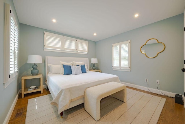bedroom with baseboards, recessed lighting, wood finished floors, and visible vents