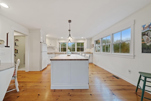 kitchen featuring butcher block counters, white refrigerator, a kitchen island, pendant lighting, and white cabinets