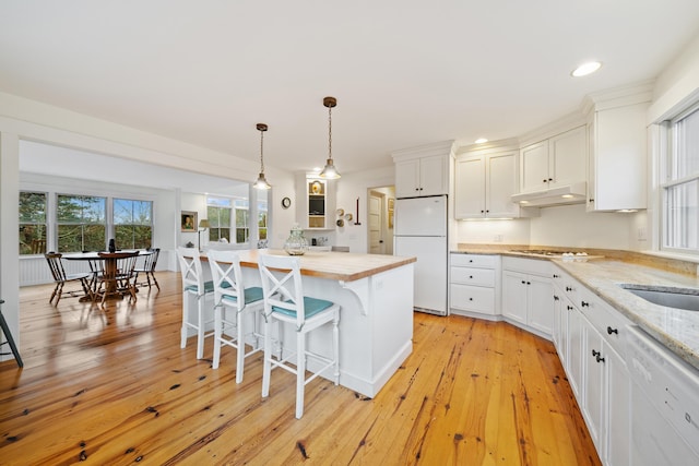 kitchen with white appliances, a breakfast bar area, light stone countertops, and white cabinets