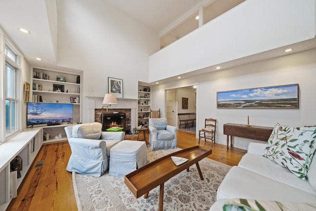 living room with built in shelves, a fireplace, a high ceiling, and light wood-type flooring