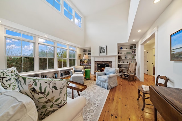 living room featuring a high ceiling, a brick fireplace, built in features, and light hardwood / wood-style flooring