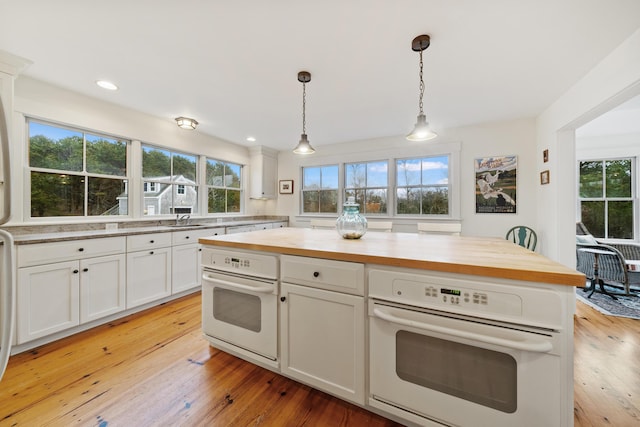 kitchen with white oven, white cabinets, light hardwood / wood-style floors, and decorative light fixtures