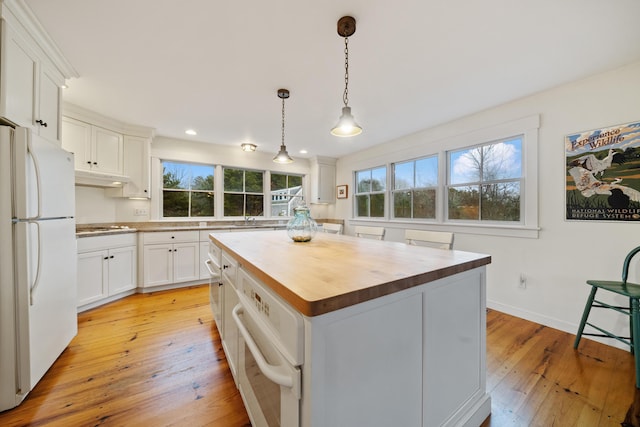 kitchen featuring wooden counters, a center island, hanging light fixtures, white appliances, and white cabinets