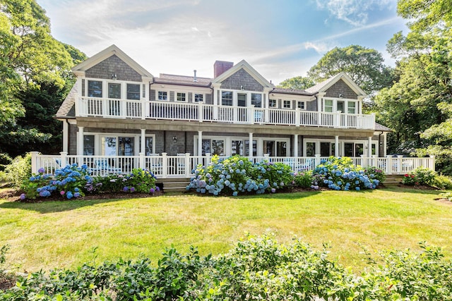 back of property with a chimney, a balcony, a deck, and a yard