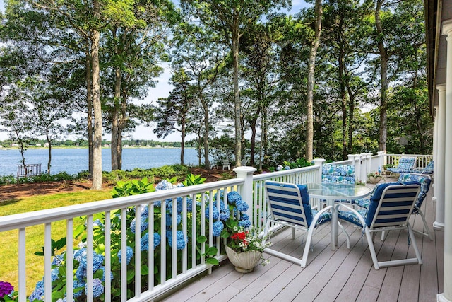 deck with a water view, outdoor dining area, and view of wooded area