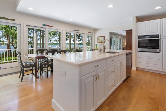 kitchen with white cabinets, oven, a sink, and an island with sink