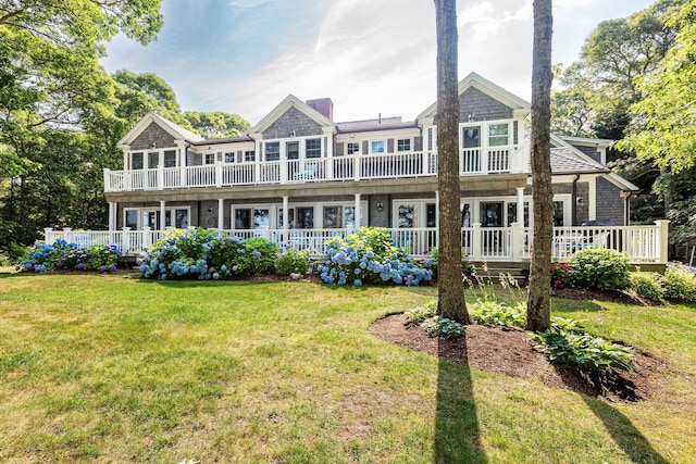 back of property with a balcony, a yard, a wooden deck, and a chimney