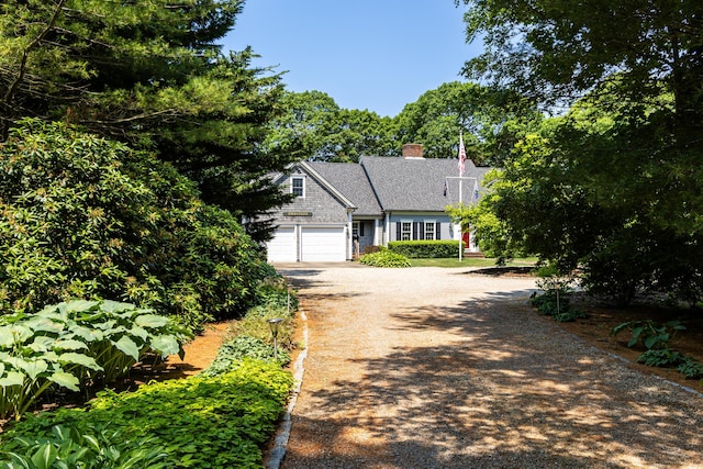 view of front facade featuring a garage, a chimney, and dirt driveway