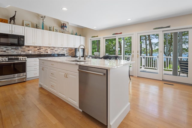 kitchen with sink, backsplash, stainless steel appliances, an island with sink, and white cabinets