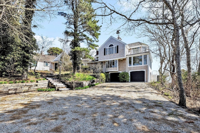 shingle-style home featuring driveway, an attached garage, a balcony, stairway, and a chimney