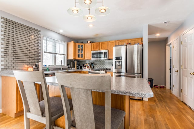 kitchen with light hardwood / wood-style flooring, a kitchen island, pendant lighting, stainless steel appliances, and backsplash