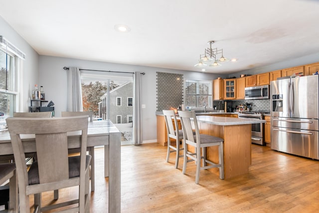 kitchen featuring pendant lighting, appliances with stainless steel finishes, a center island, decorative backsplash, and light wood-type flooring