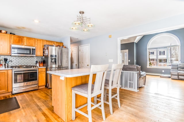 kitchen with pendant lighting, a breakfast bar, appliances with stainless steel finishes, tasteful backsplash, and light hardwood / wood-style floors