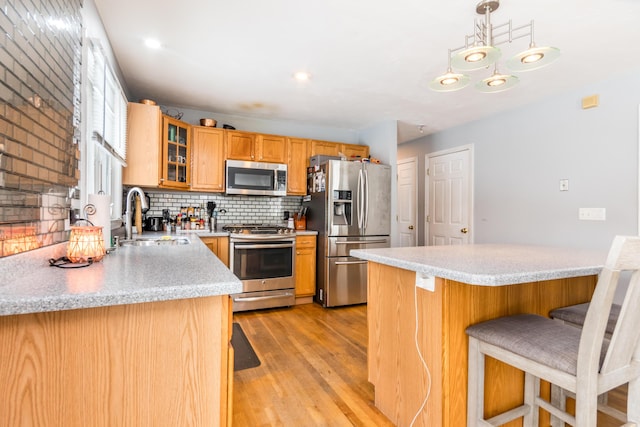 kitchen with sink, light hardwood / wood-style flooring, stainless steel appliances, decorative backsplash, and decorative light fixtures