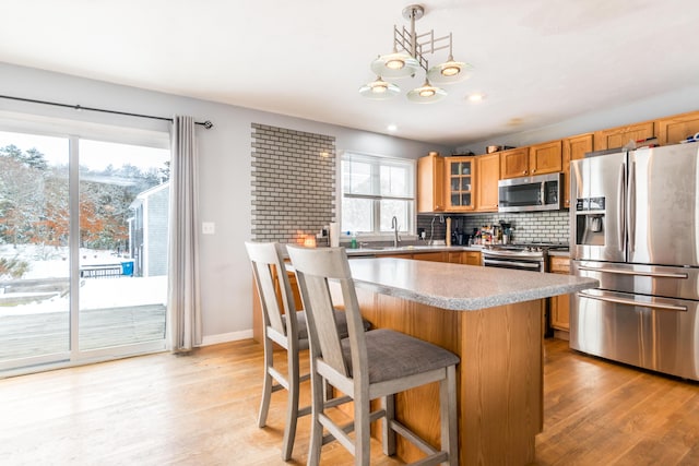 kitchen with stainless steel appliances, light hardwood / wood-style floors, decorative backsplash, a kitchen island, and decorative light fixtures