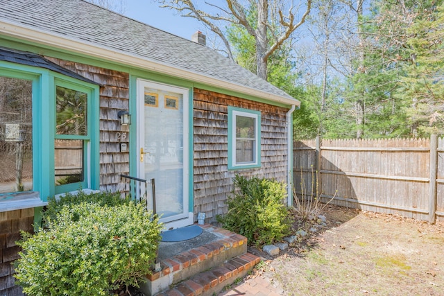 exterior space featuring roof with shingles, fence, and a chimney