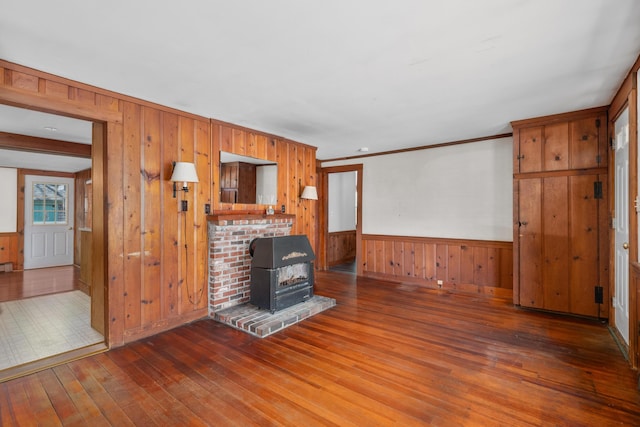 unfurnished living room with ornamental molding, a wood stove, wainscoting, wood walls, and hardwood / wood-style floors