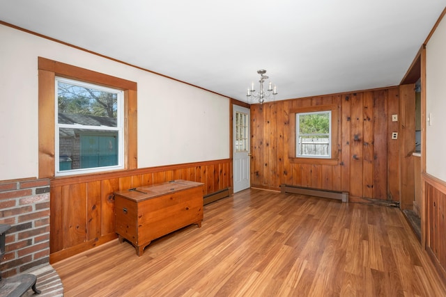 interior space with light wood-type flooring, a baseboard heating unit, wooden walls, and an inviting chandelier