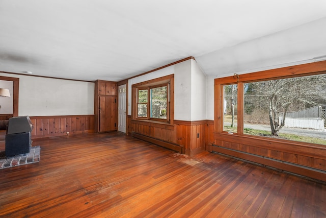 unfurnished living room featuring hardwood / wood-style floors, a baseboard heating unit, wooden walls, and wainscoting