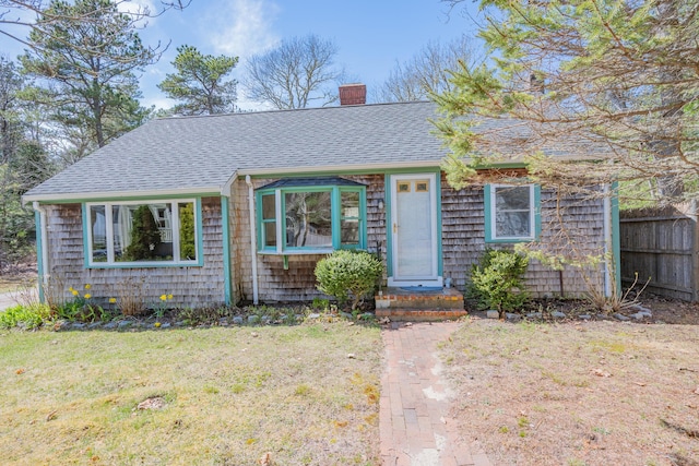 view of front of house with fence, a front lawn, a chimney, and a shingled roof