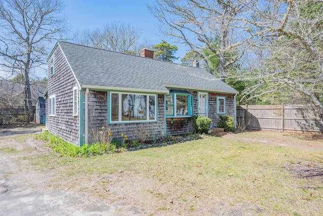 view of front facade featuring roof with shingles, a front lawn, fence, and a chimney