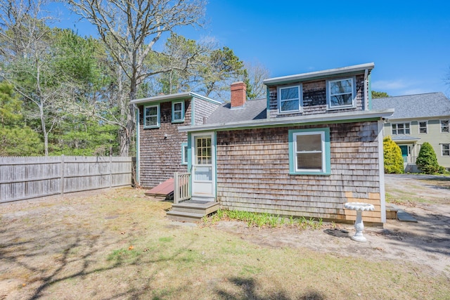 back of house featuring roof with shingles, a chimney, entry steps, fence, and a lawn