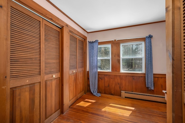 unfurnished bedroom with two closets, wood walls, baseboard heating, wood-type flooring, and a wainscoted wall